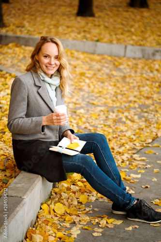Creative woman with paper notebook and coffee in golden autumn park
