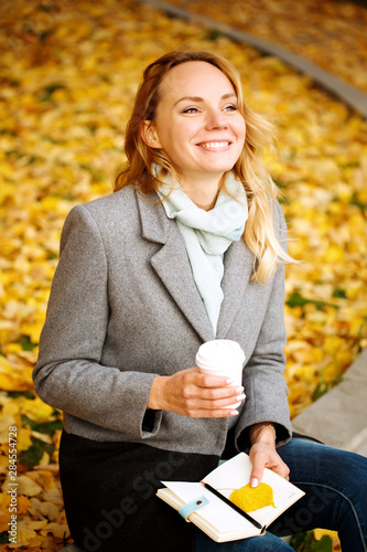 Happy creative woman with paper notebook and coffee drink outdoors