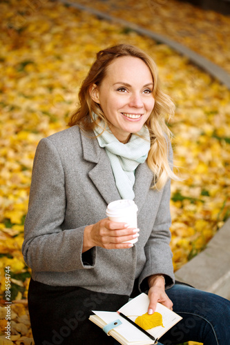 Happy blonde  smiling woman with paper notebook and coffee drink outdoors