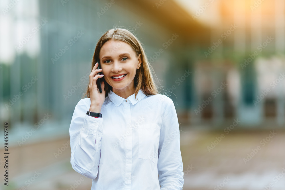 Young famale calling on a smartphone. Attractive businesswoman talking by phone. Office building Background. Technology internet and happy people concept.