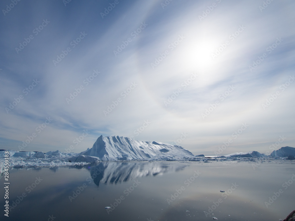 Fototapeta premium Ilulissat Icefjord in Greenland. Dramatic sun halo over glacier reflected in sea water at the Sermeq Kujalleq sea mouth
