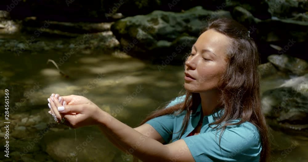 Portrait of a young dark-haired girl who is near the stream and stones. She picks up natural water in her hands and pulls them up. Portrait of a young dark-haired girl who is near the stream and stones. She picks up natural water in her hands and pulls them up.