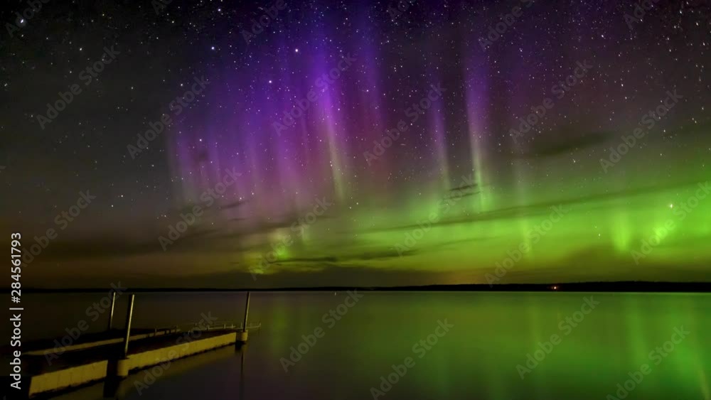 Time lapse of vivid Aurora (Northern Lights) over a calm reflecting lake with a dock in the foreground