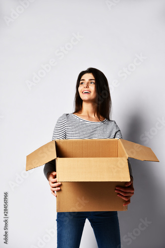 beautiful brunette woman standing on a light background with a moving cardboard box © FAB.1