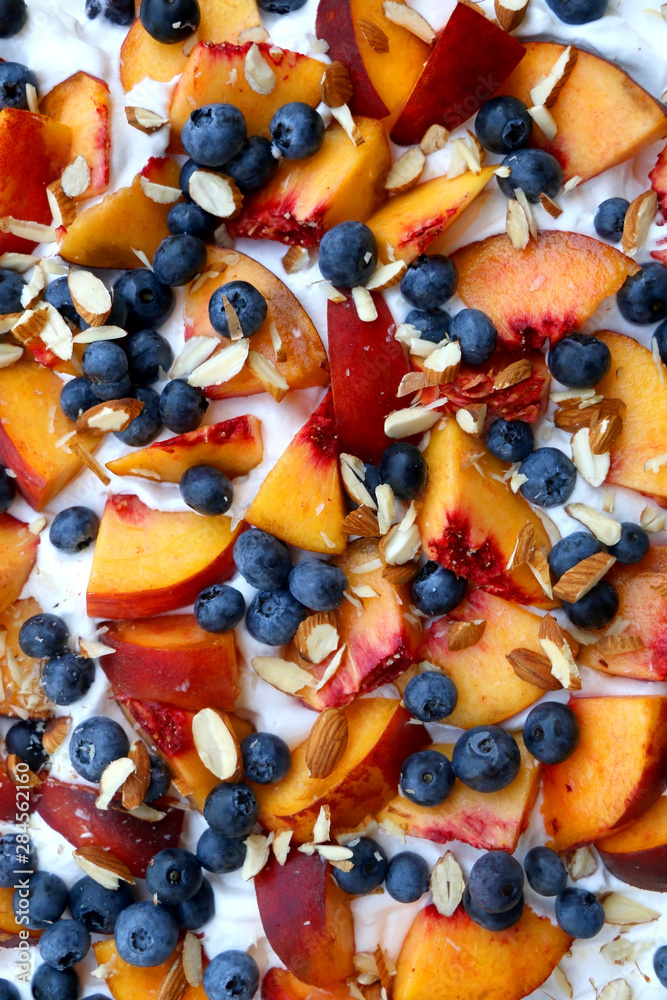 Chocolate Pavlova cake with whipped cream, peaches, blueberries and almonds. Top view.