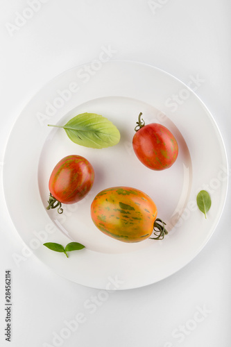 Fresh ripe tomatoes and fresh basil herb in a ceramic white plate on a white table. White background.