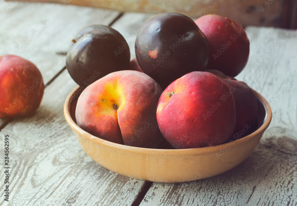 Ripe peaches and plums in a plate on a rustic background