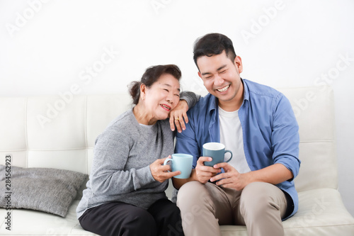 Asian senior grand mother and son drinking coffee and talking happy and smile face in living room