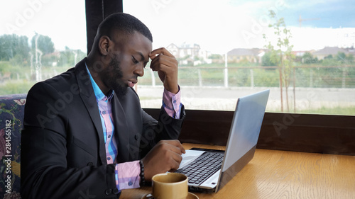 Fotografie Afro american businessman tries to type on computer sitting in cafe
