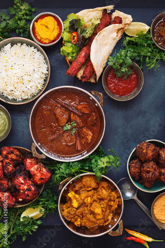 Various Indian dishes featuring  rogan josh, chicken tikka masala,tandoori chicken wings  and  kebabs, with rice and naan bread, top view