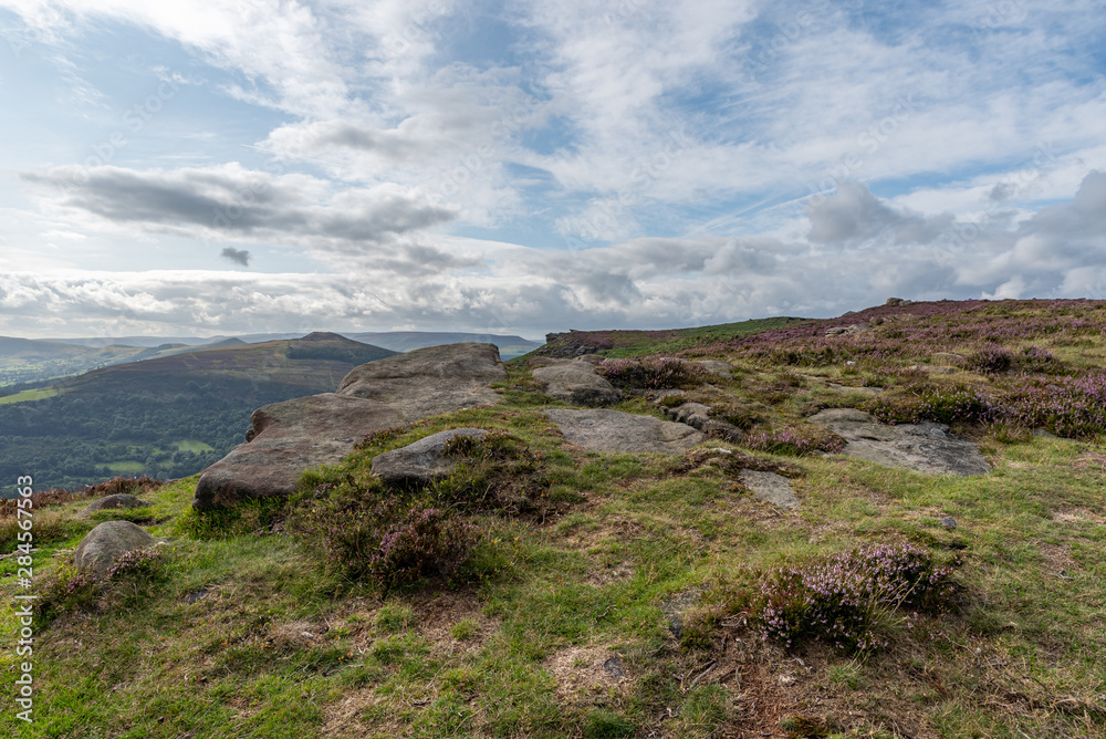 Bamford Edge Peak District view looking across to Win Hill with blue skies, fluffy clouds, and purple heather.