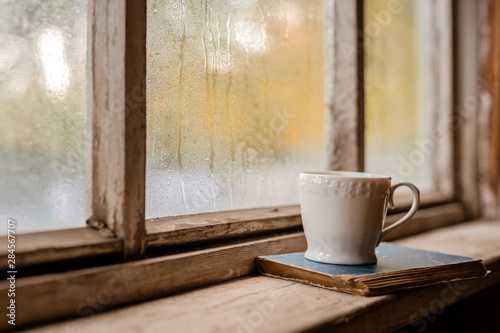 A white Cup and old books on the background of a rustic wooden wet window photo