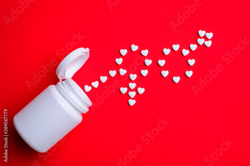 Heart pills in shape of male and female near white plastic bottle on red table. Concept of sexual problems, male sexual dysfunction, problem of potency