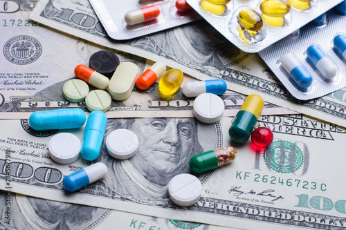 Different colorful pills capsules on money bills. Concept of expensive treatment, medicine, medical insurance.