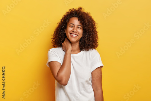 Happy lifestyle concept. Pleasant looking funny Afro woman feels lucky and satisfied, laughs happily, has white teeth with small gap, enjoys awesome day off, stands against yellow background