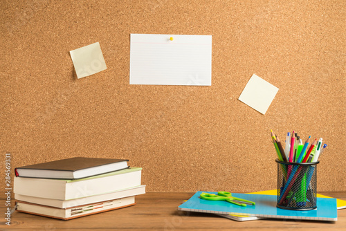 Books, notebooks and school supplies on wooden boards with a cork board in the background.