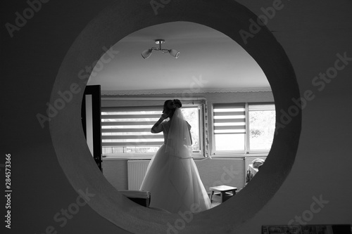 The bride stands in a round window with her back. Black and white.