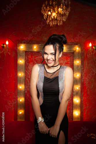 Cheerful young woman wearing party dress in red fashion room with light bulbs photo