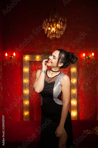 Cheerful young woman wearing party dress in red fashion room with light bulbs photo