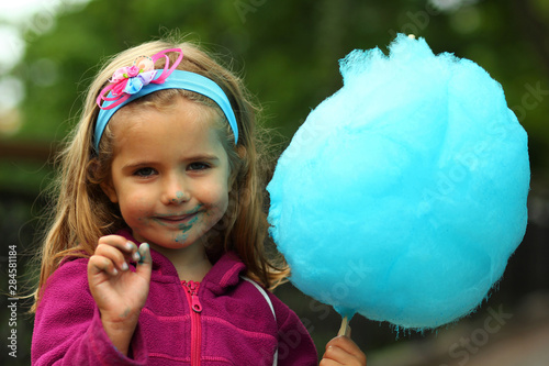 Closeup portrait of happy toddler girl eating bright blue cotton candy