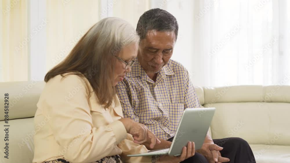 Senior couple sitting on the sofa while using a laptop computer together at home. Shot in 4k resolution Senior couple sitting on the sofa while using a laptop computer together at home. Shot in 4k resolution