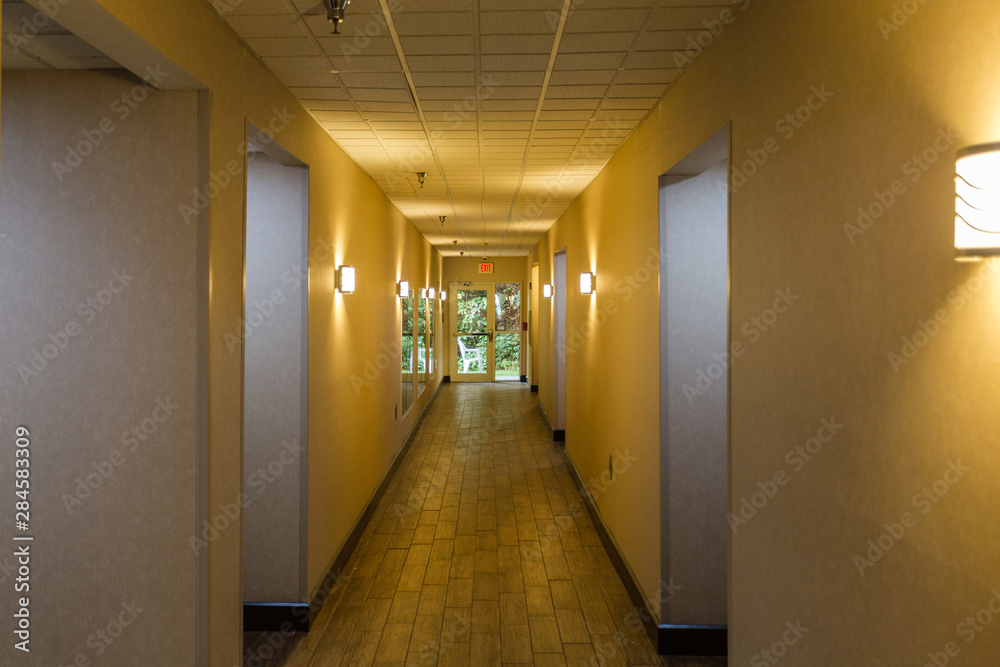 Long yellow light hallway leading outside to green bushes