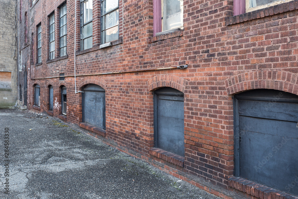 Angled view of red brick wall with windows in alley