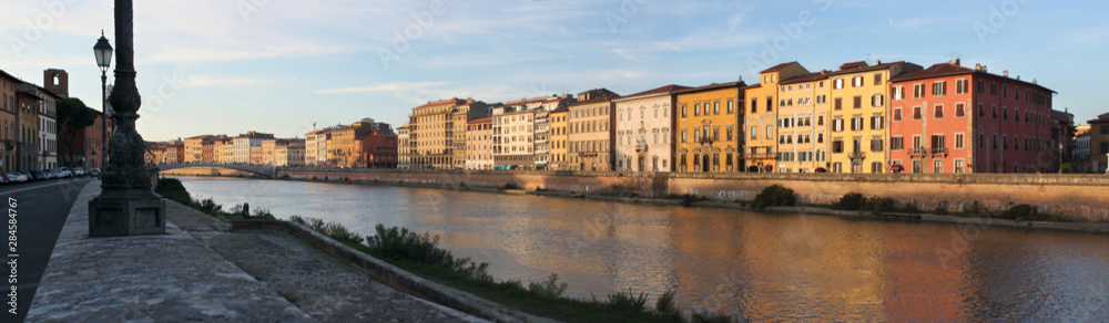 Panoramic view of Arno river with palazzo facades in Pisa, Italy, on a sunny evening