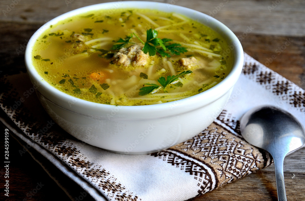 Homemade soup with meatballs and noodles, folk napkin on a wooden table. Homemade soup with meatballs and noodles, folk napkin on a wooden table.