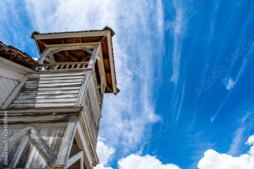 A weathered wood bell tower on an old church reaches to a vivid blue sky streaked with clouds. 