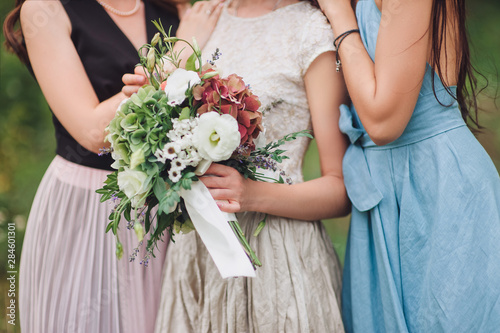 Bride and girlfriend hugging and holding a wedding bouquet of wild flowers in their hands in close-up. Friends at the wedding. Wedding details. photo