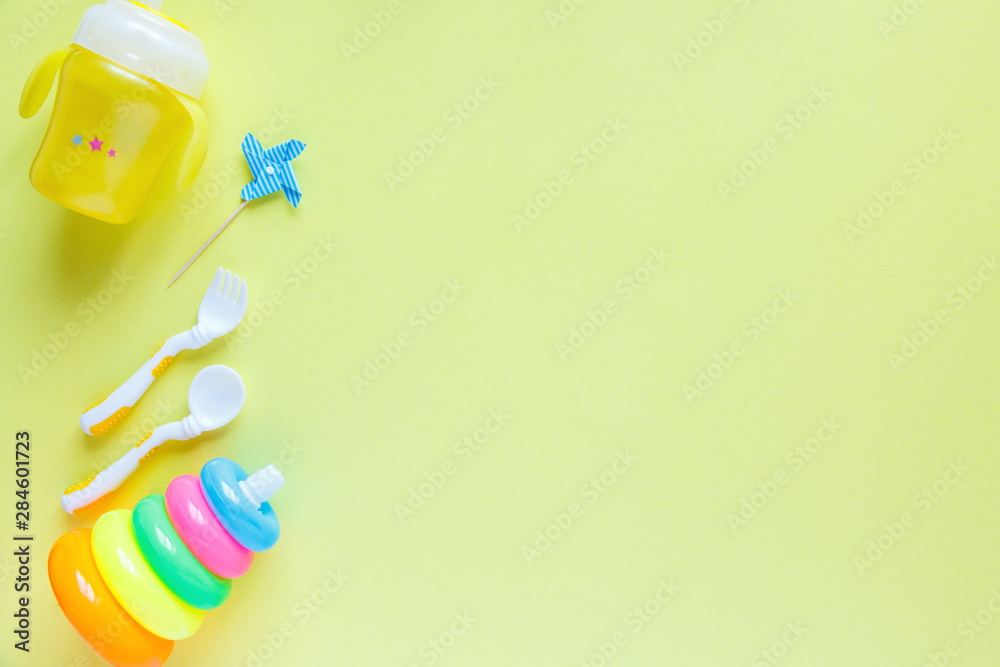 Baby care accessories background:  bottle, pyramid and toys on yellow background with copy space; top view, flat lay
