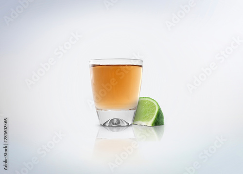 Gold shot of tequila. Alcoholic distilled beverage with slice of lemon / lime on the side. Isolated on white background.