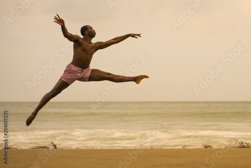 contemporary dance choreographer doing ballet beach workout . young attractive and athletic black African American man dancing on sunrise jumping elegant