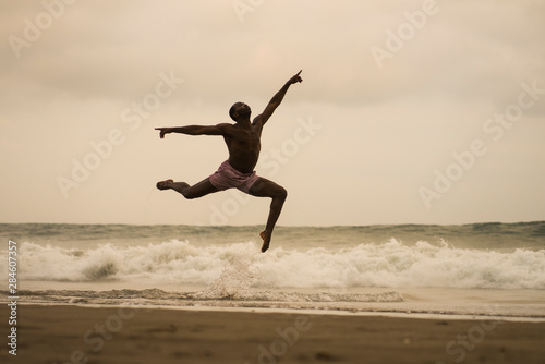 contemporary dance choreographer doing ballet beach workout . young attractive and athletic black African American man dancing on sunrise jumping elegant