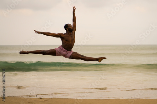 contemporary dance choreographer doing ballet beach workout . young attractive and athletic black African American man dancing on sunrise jumping elegant