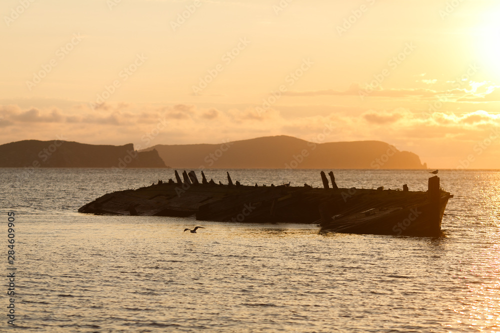 Old abandoned skeleton of a wooden ship half sunken in the sea against the backdrop of a beautiful sunset
