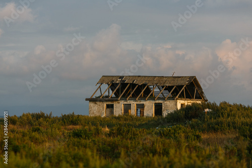 Old abandoned house with broken windows and a roof among tall grass