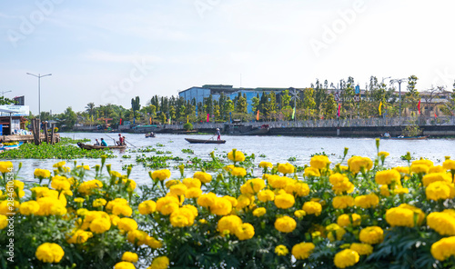 Ferryman rowing takes visitors across river to visit floating market with foreground marigold, this is main transportation Lunar New Year in Soc Trang, Vietnam