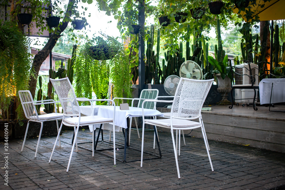 White chairs and table set outdoor coffee shop in the green garden White chairs and table set outdoor coffee shop in the green garden