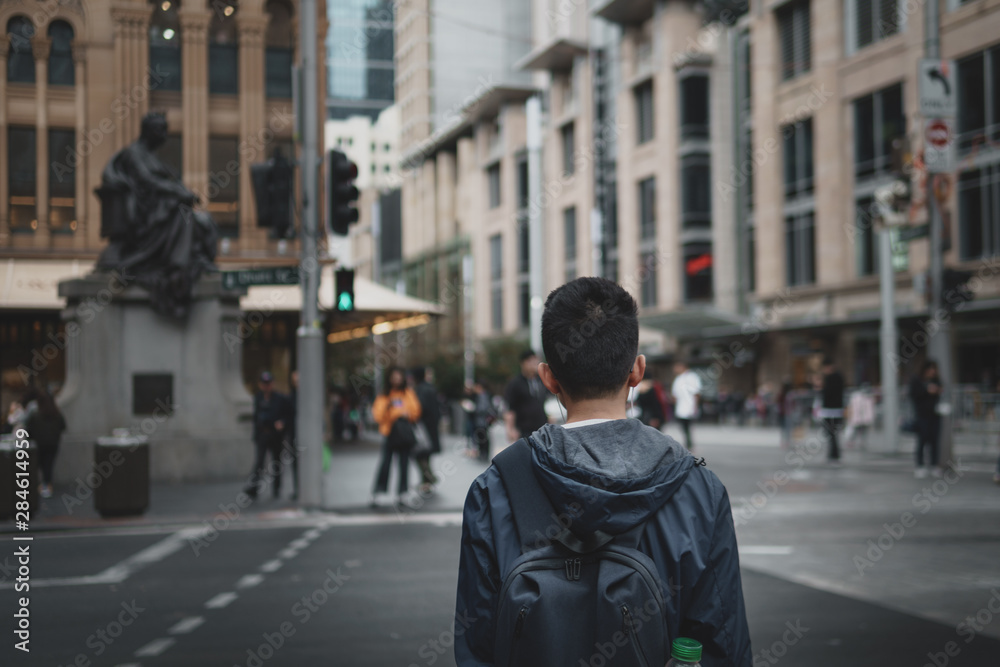 Young man with headphones in waiting to cross the road in the city.
