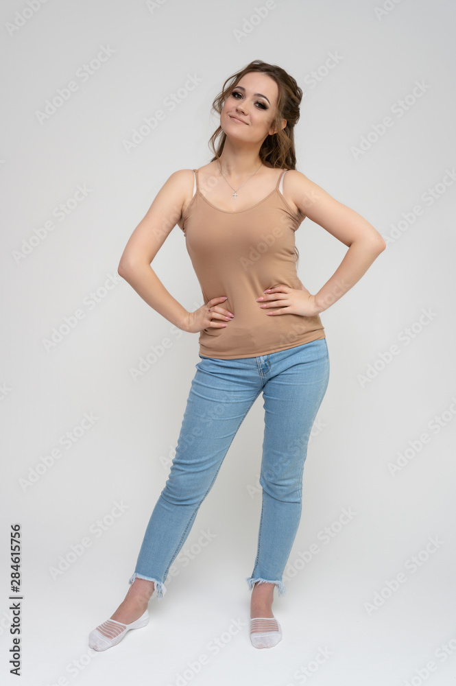 Photo full-length portrait of a pretty brunette woman girl with long beautiful curly hair on a white background in a t-shirt and blue jeans. Talking while standing in front of the camera. Photo full-length portrait of a pretty brunette woman girl with long beautiful curly hair on a white background in a t-shirt and blue jeans. Talking while standing in front of the camera.