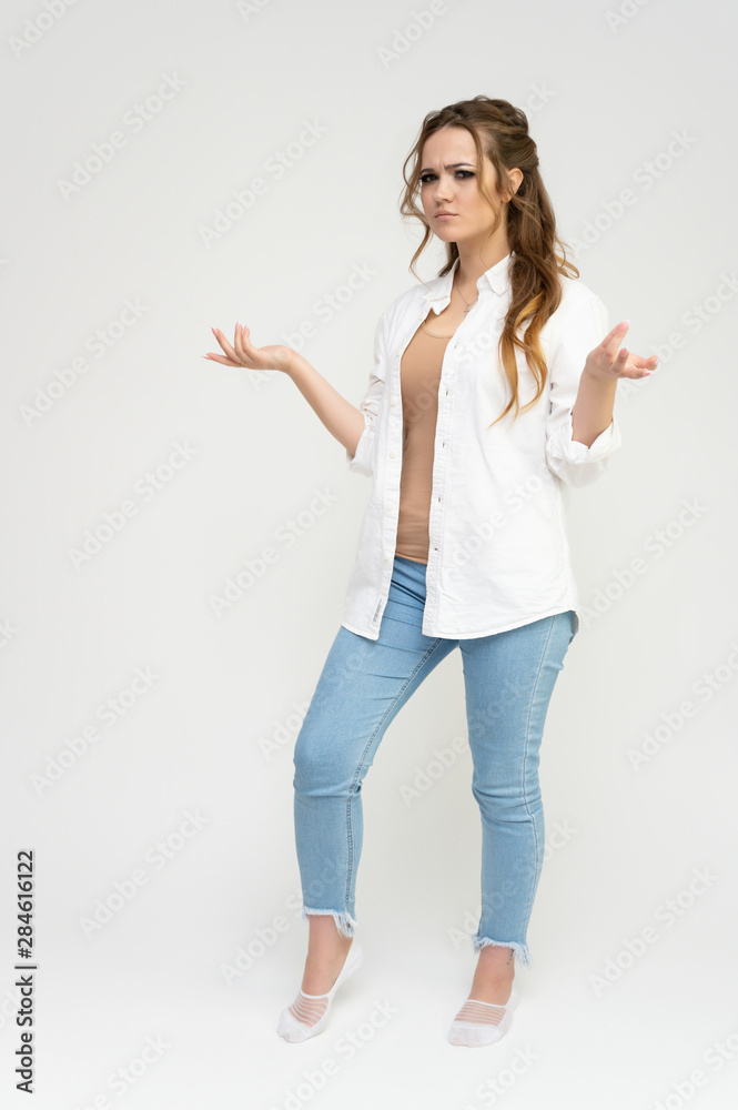 Photo full-length portrait of a pretty brunette woman girl with long beautiful curly hair on a white background in a white shirt and blue jeans. Talking while standing in front of the camera.