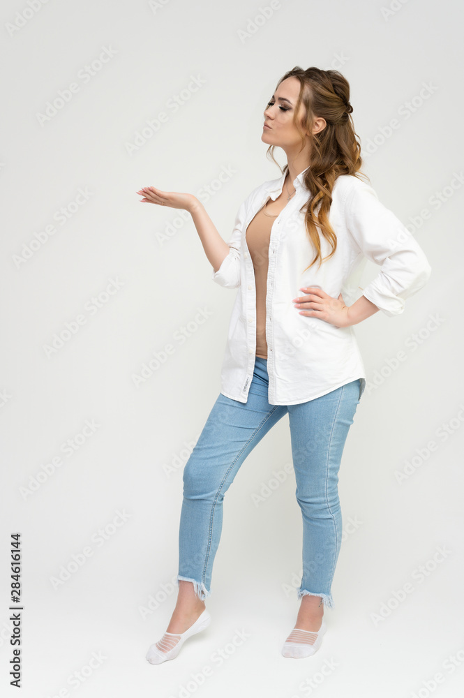 Photo full-length portrait of a pretty brunette woman girl with long beautiful curly hair on a white background in a white shirt and blue jeans. Talking while standing in front of the camera.