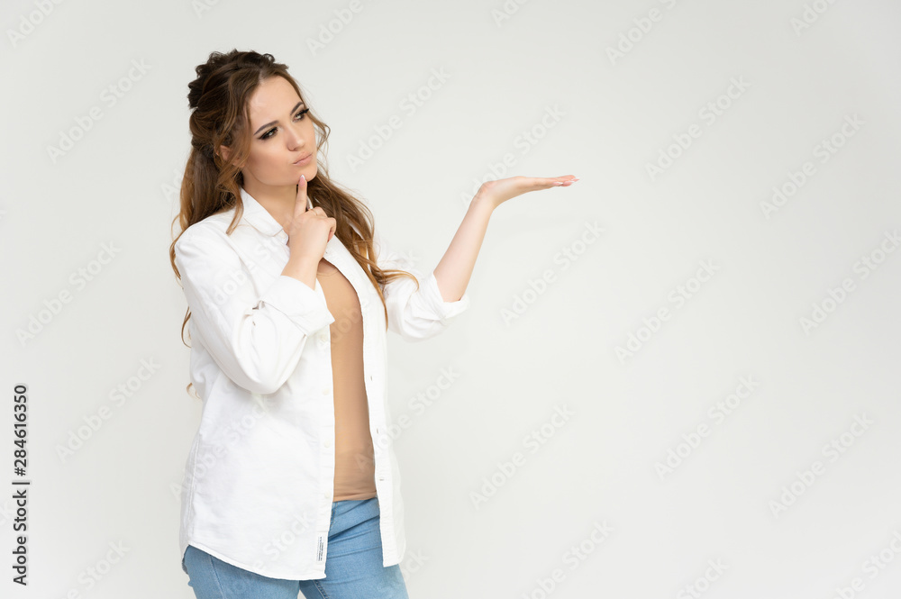 Photo portrait above the knee of a pretty brunette woman girl with long beautiful curly hair on a white background in a white shirt and blue jeans. Talking while standing in front of the camera. Photo portrait above the knee of a pretty brunette woman girl with long beautiful curly hair on a white background in a white shirt and blue jeans. Talking while standing in front of the camera.