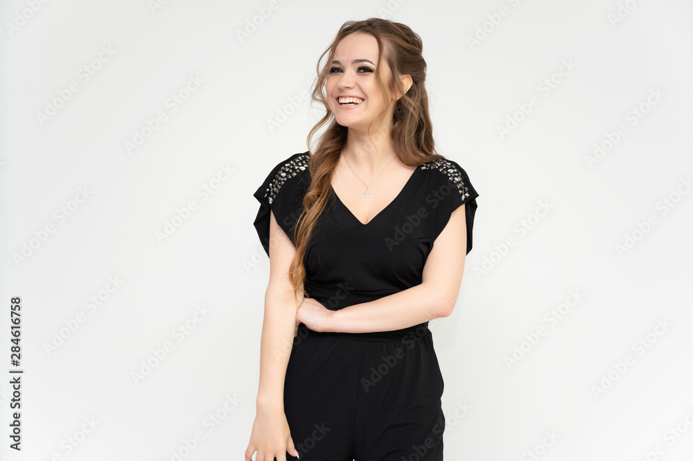 Photo portrait above the knee of a pretty girl of a brunette woman with long beautiful curly hair on a white background in a black dress. Talking while standing in front of the camera. Photo portrait above the knee of a pretty girl of a brunette woman with long beautiful curly hair on a white background in a black dress. Talking while standing in front of the camera.