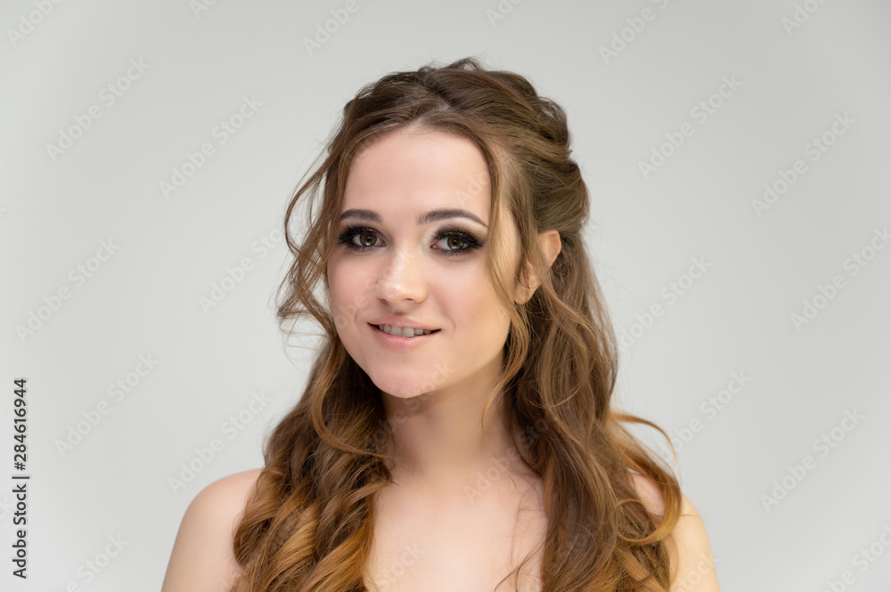 Close-up photo portrait of a pretty brunette woman girl with long beautiful curly hair on a white background. Standing in front of the camera