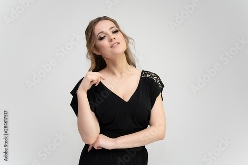 Photo waist-length portrait of a pretty brunette woman girl with long beautiful curly hair on a white background in a black dress. Talking in different poses. Standing facing the camera.