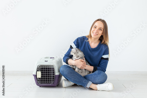 Charming positive young woman holds in her hands her beautiful gray fold scottish cat sitting on the floor in a new apartment. Pet concept.