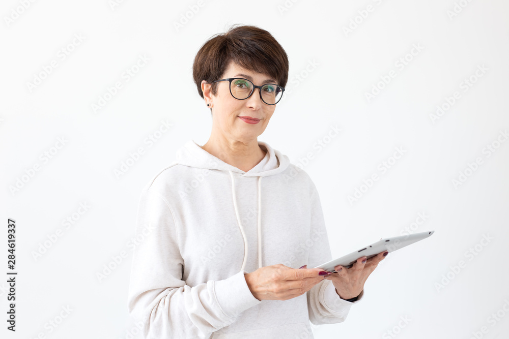 Technologies and modern people concept - Beautiful woman 50 years old with short hair holding tablet in light room Technologies and modern people concept - Beautiful woman 50 years old with short hair holding tablet in light room